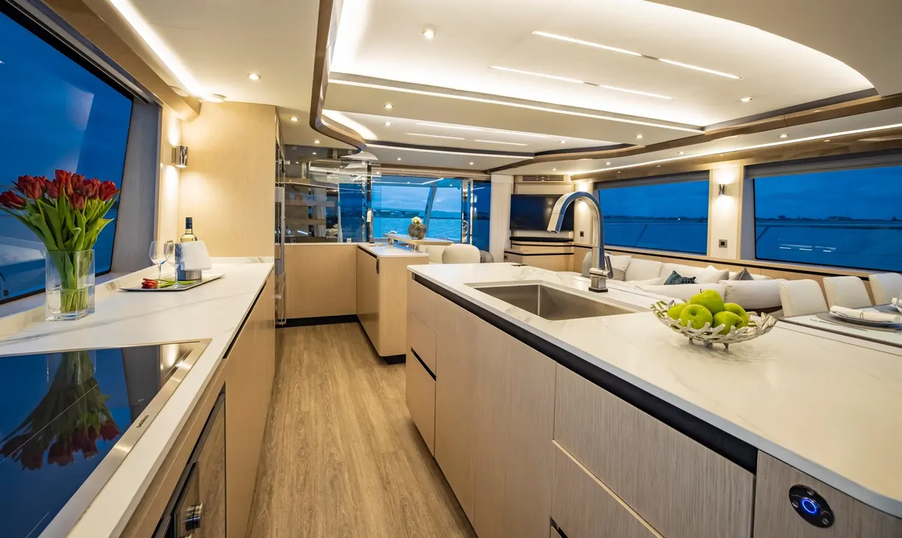 Modern yacht interior featuring a stylish kitchen, polished surfaces, a vase of tulips, and panoramic water views at dusk.